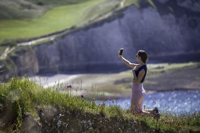 Woman talking selfie while kneeling against sea