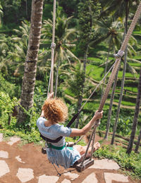 Rear view of girl sitting on swing in forest