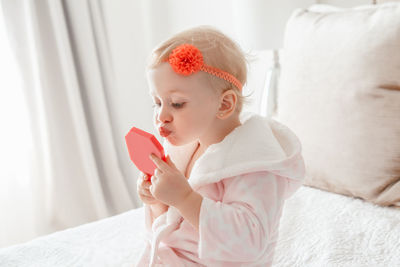 Cute girl applying make-up while sitting on bed at home