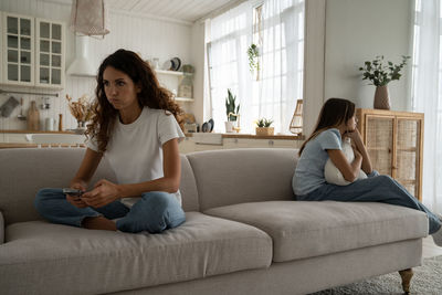 Exhausted tired mother of difficult teenager sitting on sofa thinking about conflict with daughter