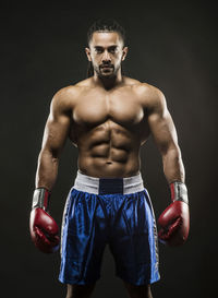 Portrait of shirtless boxer standing against black background