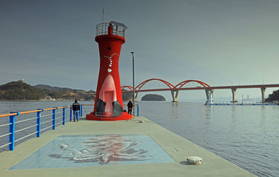 Lighthouse by sea against clear sky