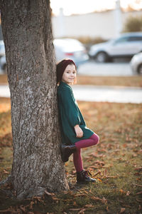 Side view of girl leaning on tree at park