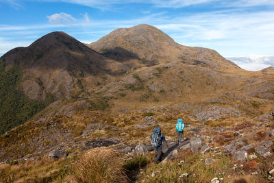 People on rocks by mountains against sky