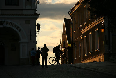 People walking in city against sky during sunset