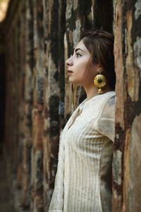 Side view of woman standing by wooden wall