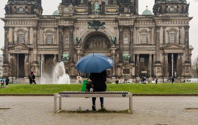 Rear view of woman sitting with umbrella on bench at berlin cathedral