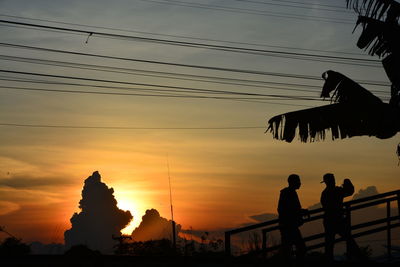 Silhouette people against orange sky during sunset