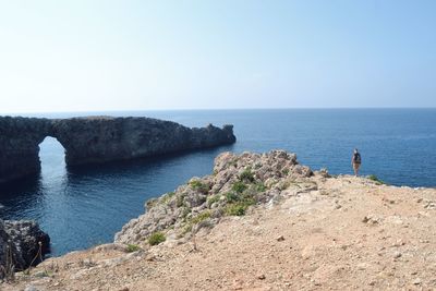 Man standing on mountain by sea against clear sky