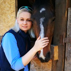 Portrait of woman petting horse in stable