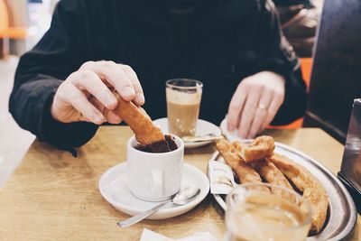 Close-up of man eating and dipping churros in chocolate in a cafeteria 