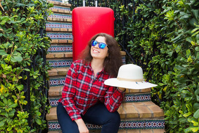 Young woman wearing sunglasses hat while standing against plants