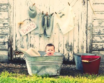 Baby in bathtub at back yard against wooden door