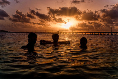 Silhouette friends swimming in sea against sky during sunset