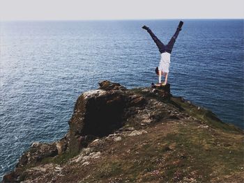 Boy doing handstand on cliff by sea