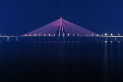 Illuminated bridge over sea against sky at night