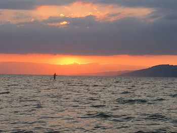 Silhouette man in sea against sky during sunset