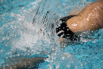 Midsection of shirtless male swimmer swimming in pool