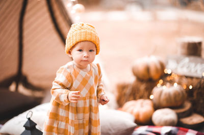 Cute baby girl 1-2 year old wearing yellow knitted hat and dress over lights at background.