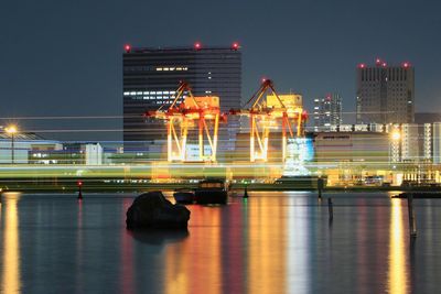 Illuminated city by river against sky at night