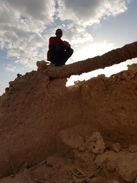 Low angle view of man sitting on rock against sky