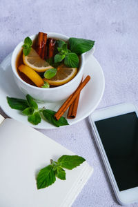 Black and green tea with lemon, cinnamon sticks and mint leaves on table with mobile phone. 