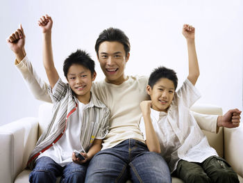 Portrait of smiling father sitting with sons against wall on sofa