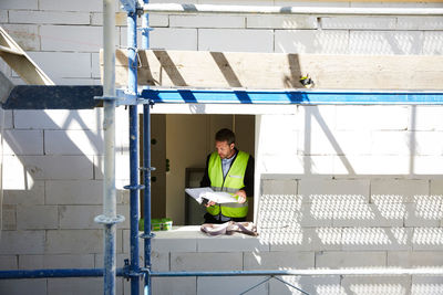 Architect analyzing blueprints while standing at incomplete building