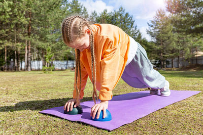 A teenage girl goes in for sports in nature, on a sunny summer day she does push-ups on a sports mat