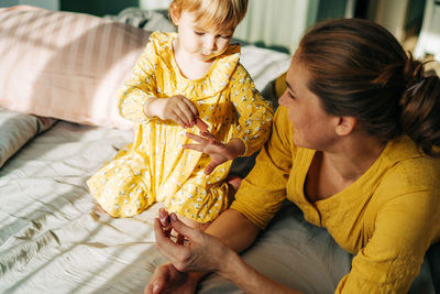 A little daughter under the supervision of her mother, paints her nails with varnish.