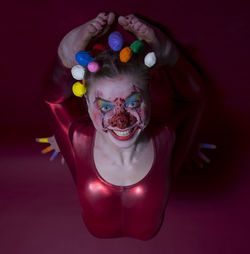 Portrait of woman with face paint wearing clown costume on colored background