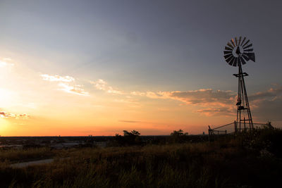 Silhouette american-style windmill on field against sky during sunset