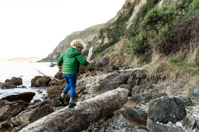 Curly haired child walking on log near ocean in new zealand