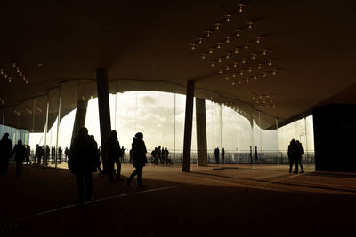 Silhouette people walking on bridge against sky in city