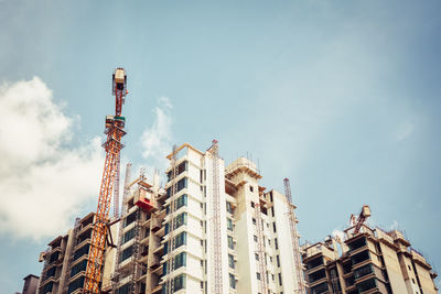 Low angle view of crane by buildings against sky