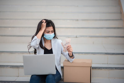 Woman using laptop by box on staircase