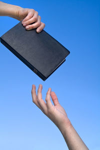 Low angle view of hand holding book against clear blue sky