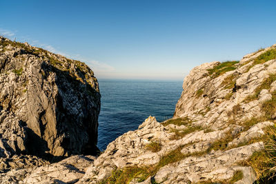 Rock formations by sea against clear blue sky