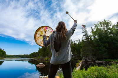 Woman holding umbrella standing by lake against sky