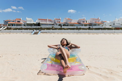 From above happy female in swimsuit lying on inflatable mattress on sandy seashore and sunbathing on sunny day during summer vacation