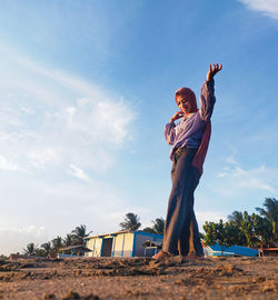 A girl is standing on the beach against the background of buildings, trees, clouds and sky