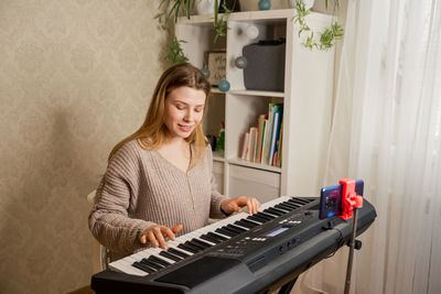 Young pretty woman at home playing on synthesizer for followers