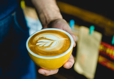 Cropped hand holding coffee in cup at cafe