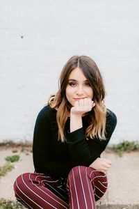Portrait of beautiful woman smiling while sitting against wall