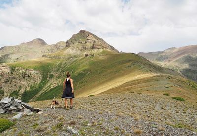 Rear view of woman with dog standing on mountain against sky