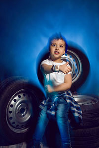 Boy in a white t shirt shirt and hat sits on a background of car wheels on a blue