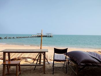 Chairs and table on beach against clear sky
