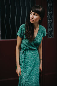 Young woman looking away while standing against wall