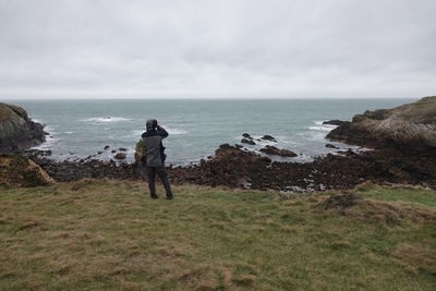 Rear view of man standing on rock by sea against sky