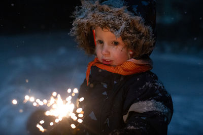 Toddler girl in winter clothes walking outside and holding sparkler in her hand. dark and snowy